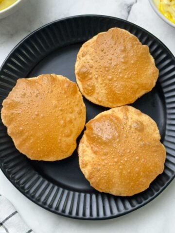 crispy and puffy poori served on a plate with potato sagu and shrikhand on the side