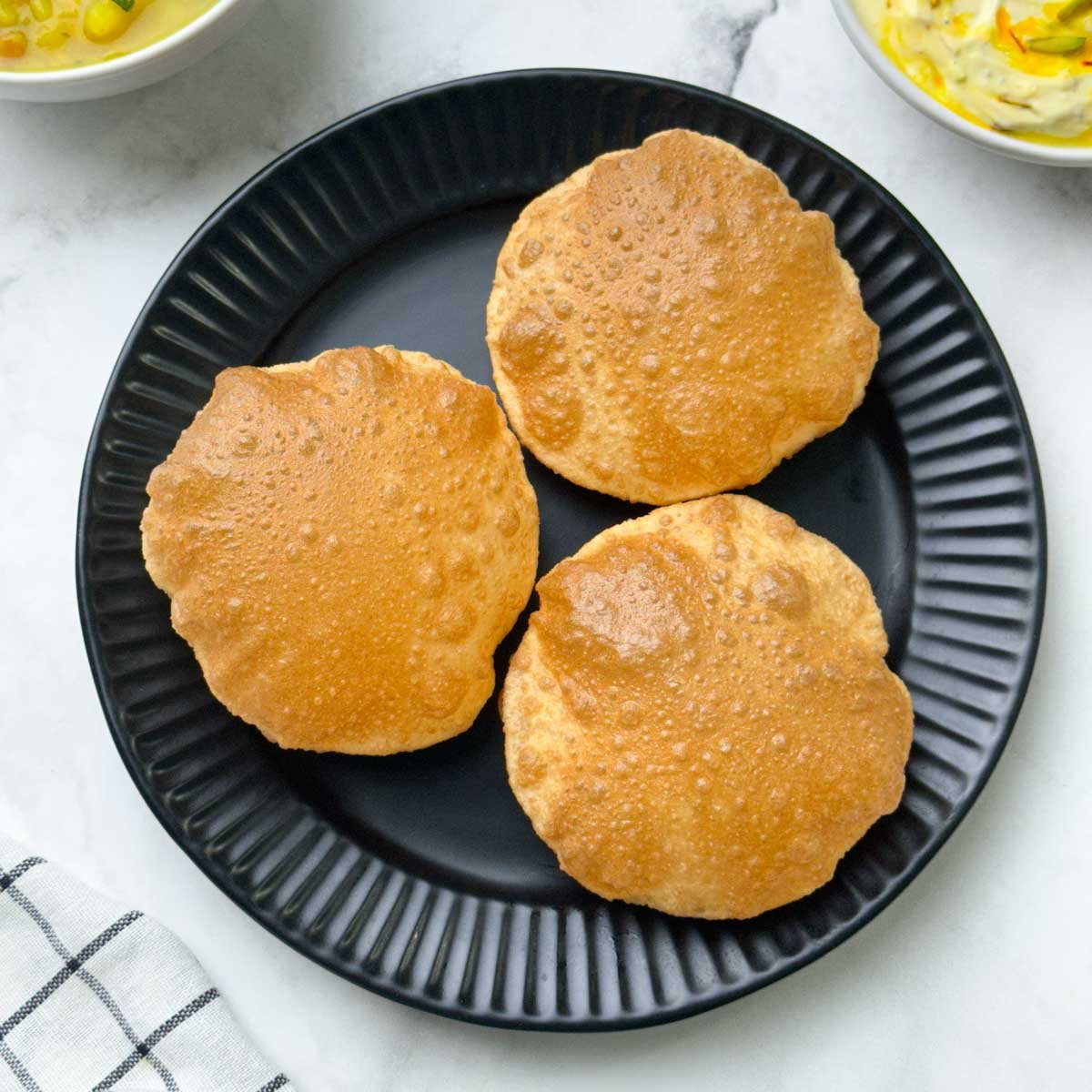 crispy and puffy poori served on a plate with potato sagu and shrikhand on the side