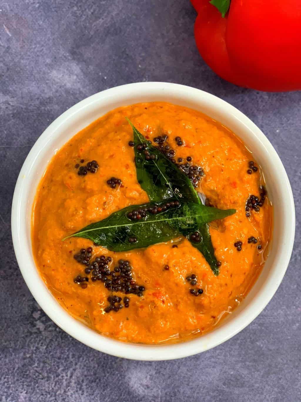 red bell pepper chutney served in a white bowl with tempering on top