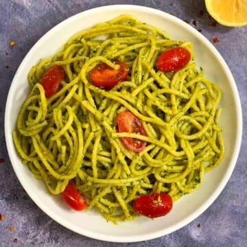 Spaghetti Pesto served on a plate with cherry tomatoes on top