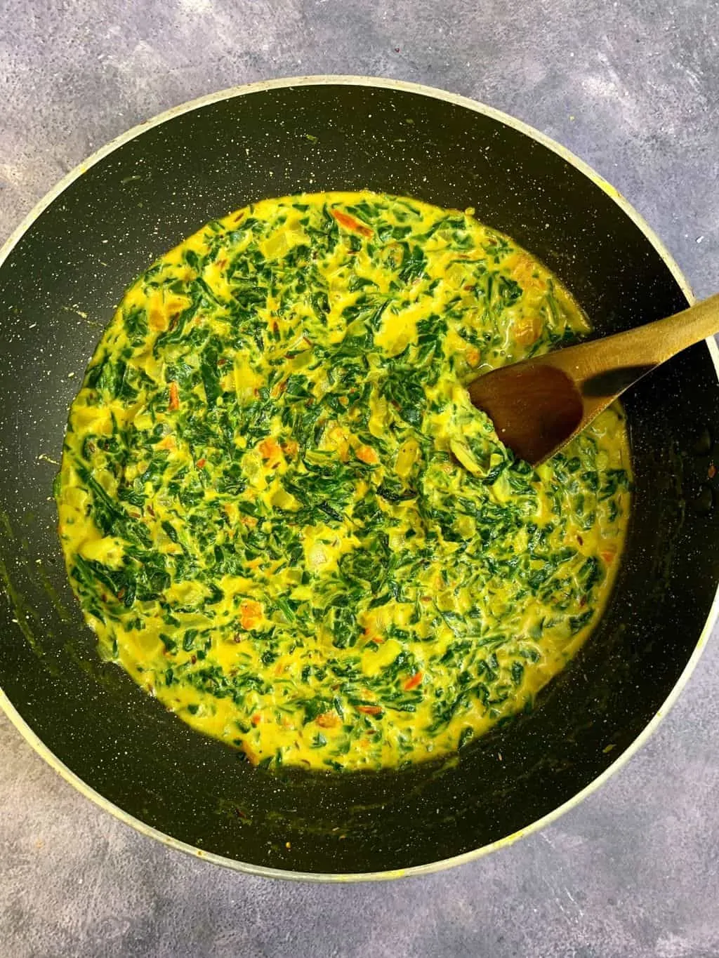 dairy free creamed spinach in a pan with a wooden spoon