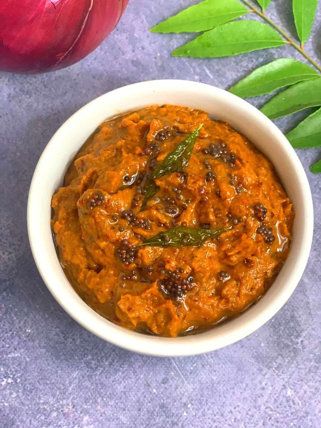 raw onion chutney served in a white bowl with curry leaves stalk on side