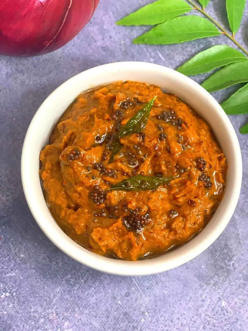 raw onion chutney served in a white bowl with curry leaves stalk on side