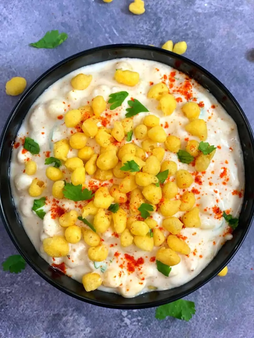 boondi raita served in a bowl topped with dry boondi cilantro and red chili powder