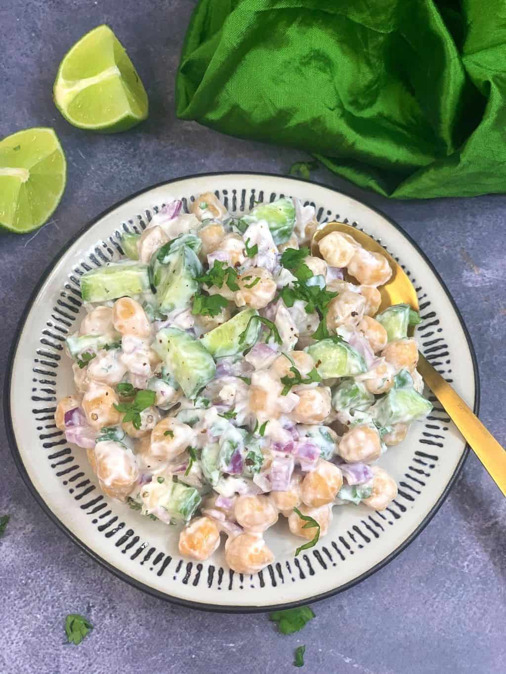 chickpea yogurt salad served in a plate with a spoon and lemon wedges on the side