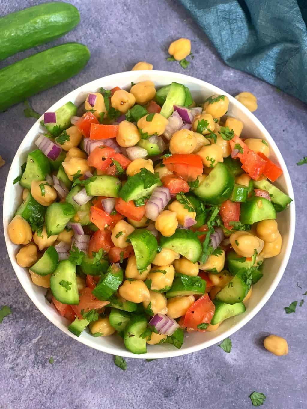 garbanzo beans salad served in a white bowl with persian cucumber on the side