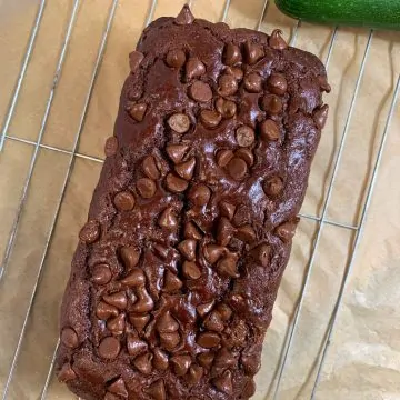 chocolate healthy zucchini bread on a wirestand with zucchini on side