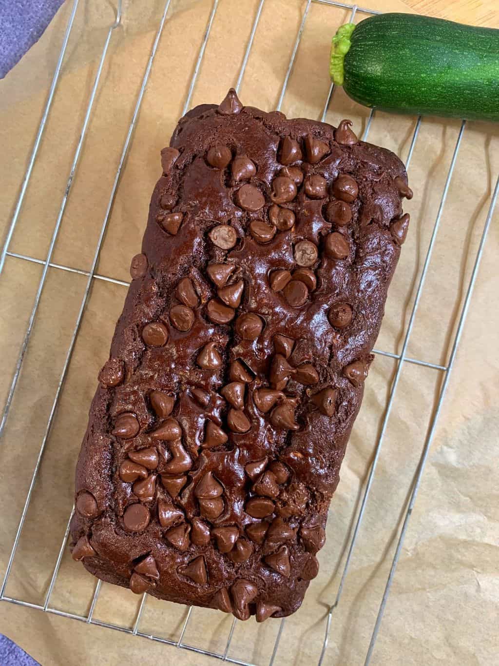 chocolate healthy zucchini bread on a wirestand with zucchini on side