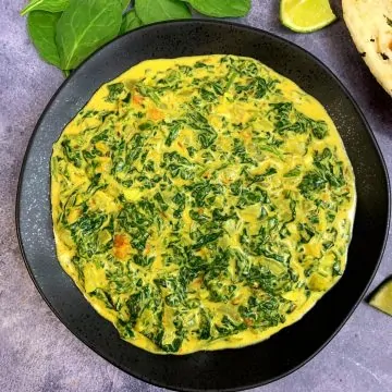 indian style creamed spinach served in a black plate with lemon wedges and naan on side