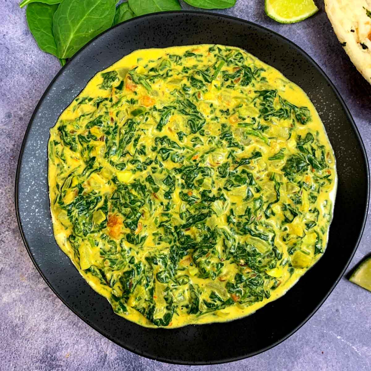 Indian Style Creamed Spinach curry served on black palte with naan on the side