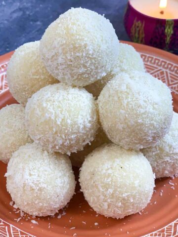 instant coconut laddos placed over one another on a plate with light candle on the side