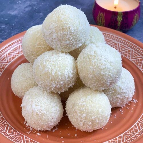 instant coconut laddos placed over one another on a plate with light candle on the side