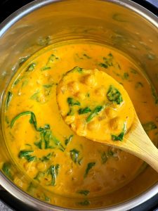 chickpea spinach curry in instant pot insert with a wooden spoon full of curry.