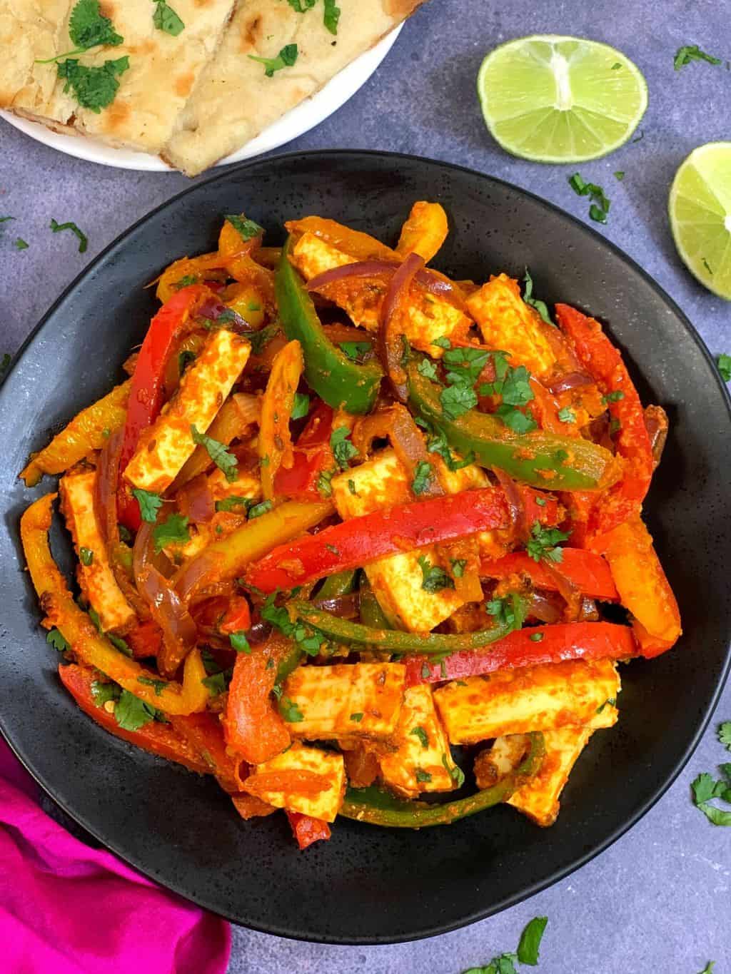 vegetable paneer jalfrezi served in a black plate with lemon wedges and naan on side