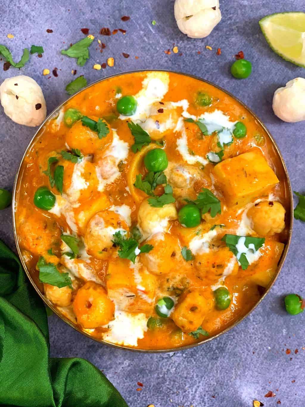 Paneer Matar Makhana Curry served in a copper bottom bowl ,lemon wedges and makhana on side 