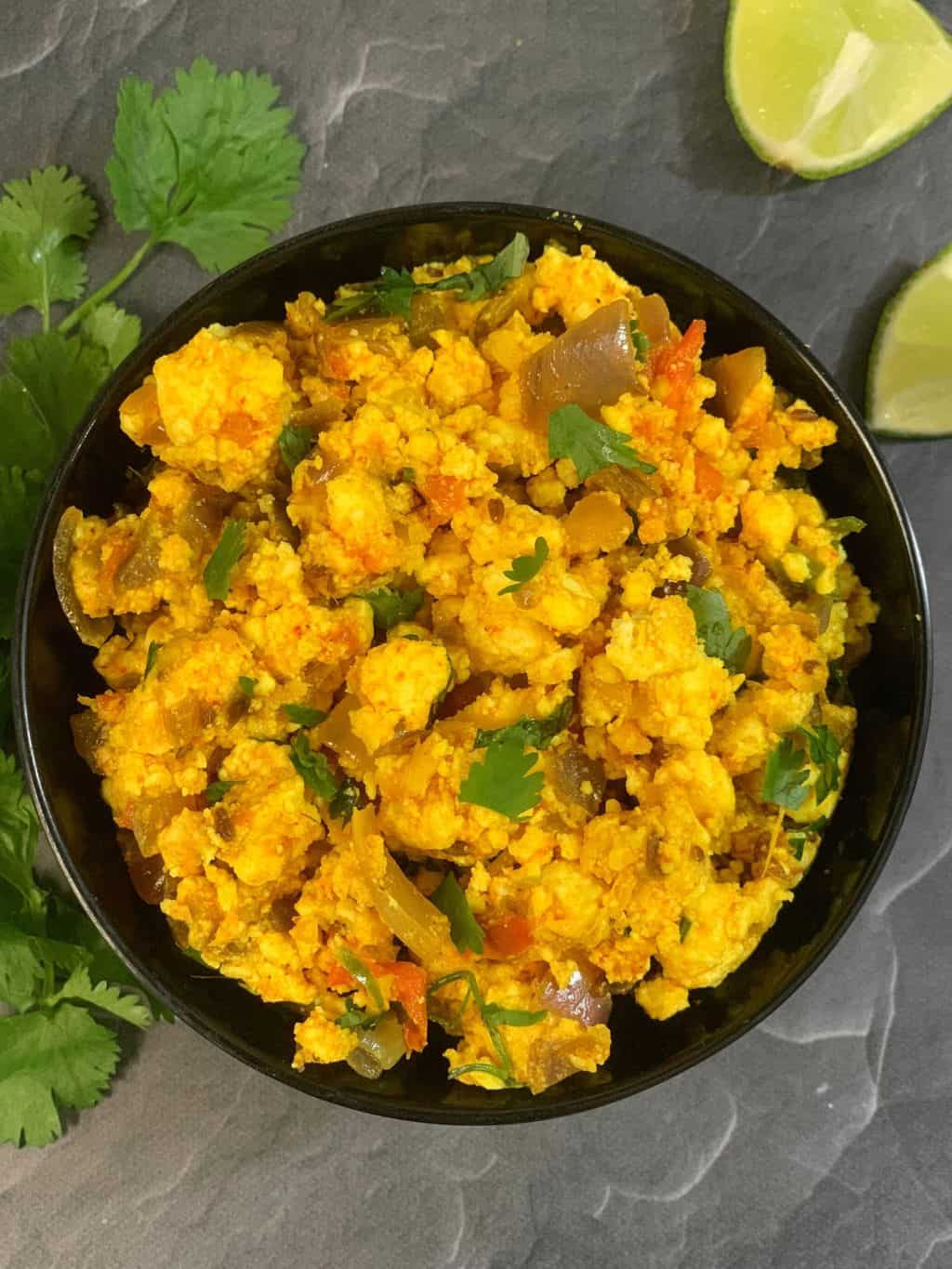 dry paneer bhurji served in a black bowl with lemon wedges and cilantro on side