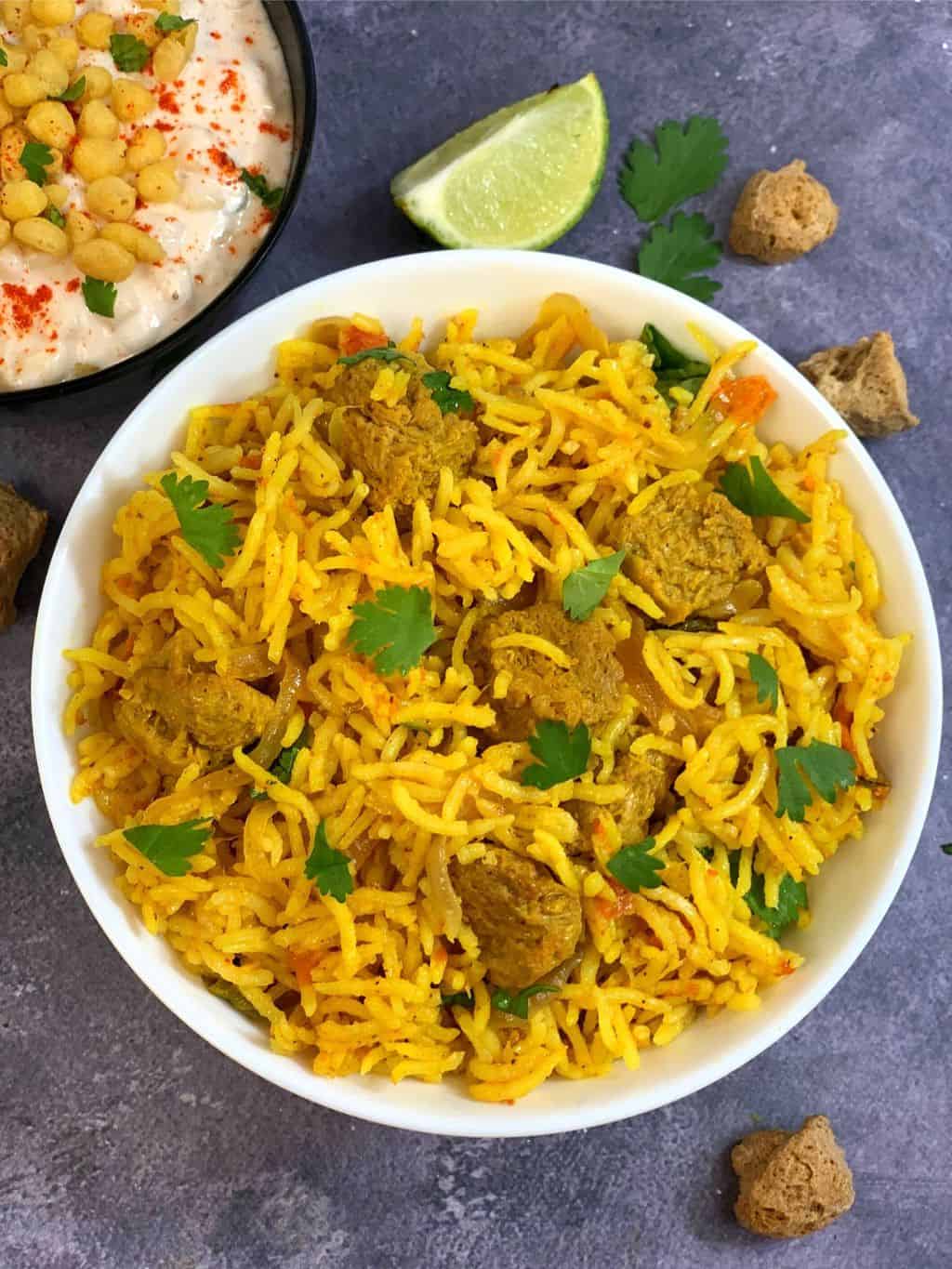 instant pot soya chunks biryani served in a white bowl with raita on side