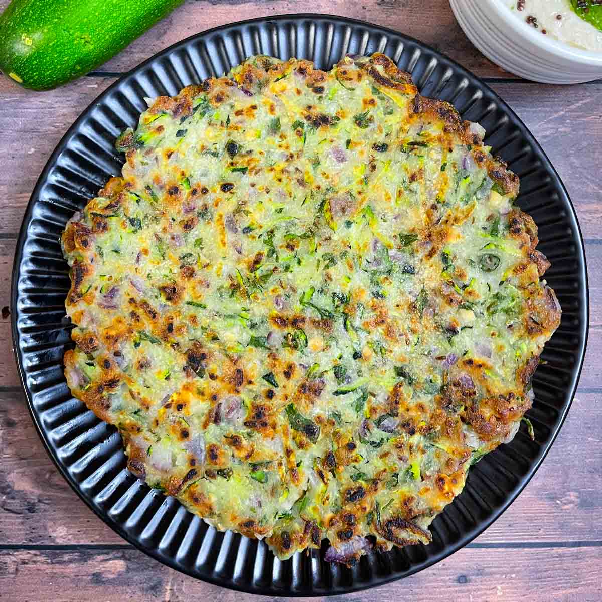 zucchini thalipettu served on a plate with coconut chutney on the side