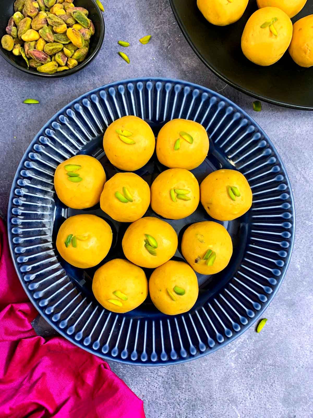 besan laddos arranged on a plate with pistachios on the side