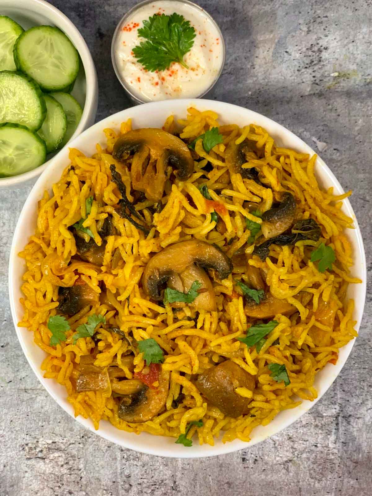 Mushroom Biryani served in a bowl with side of cucumber and raita