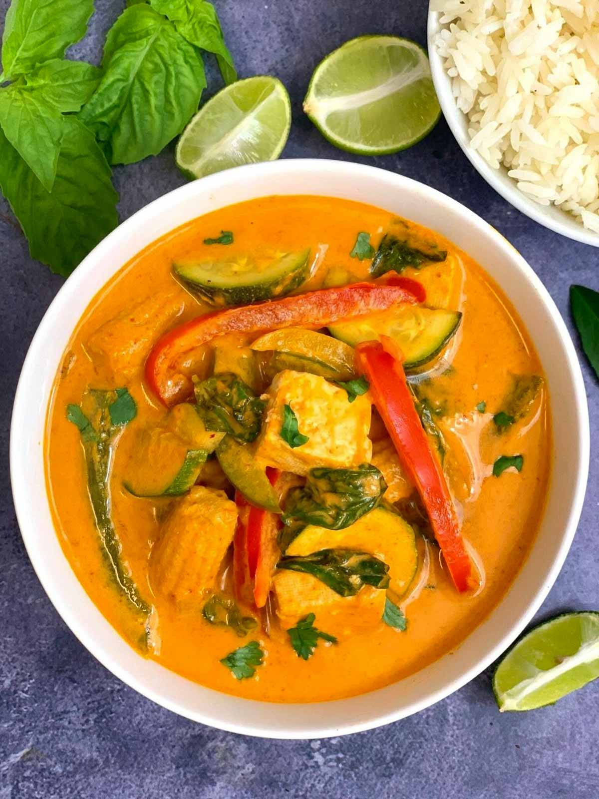 thai red curry served in a white bowl garnished with cilantro and jasmine rice lemon wedges on side