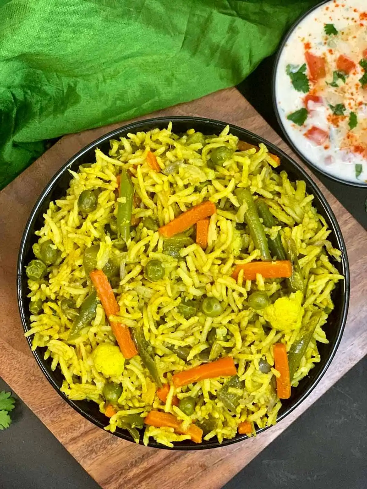 Vegetabilsk pulao serveret i en sort skål og tomatløg raita på siden