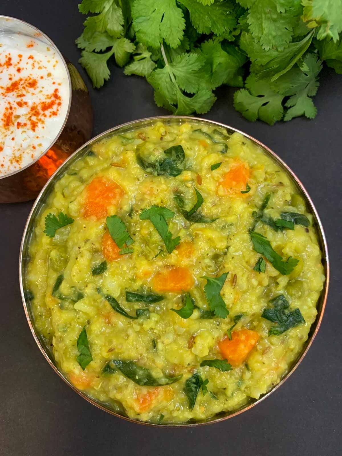 Bajra Khichdi also known as bajre ki khichdi served in a steel bowl garnished with coriander leaves with raita and cilantro on the side