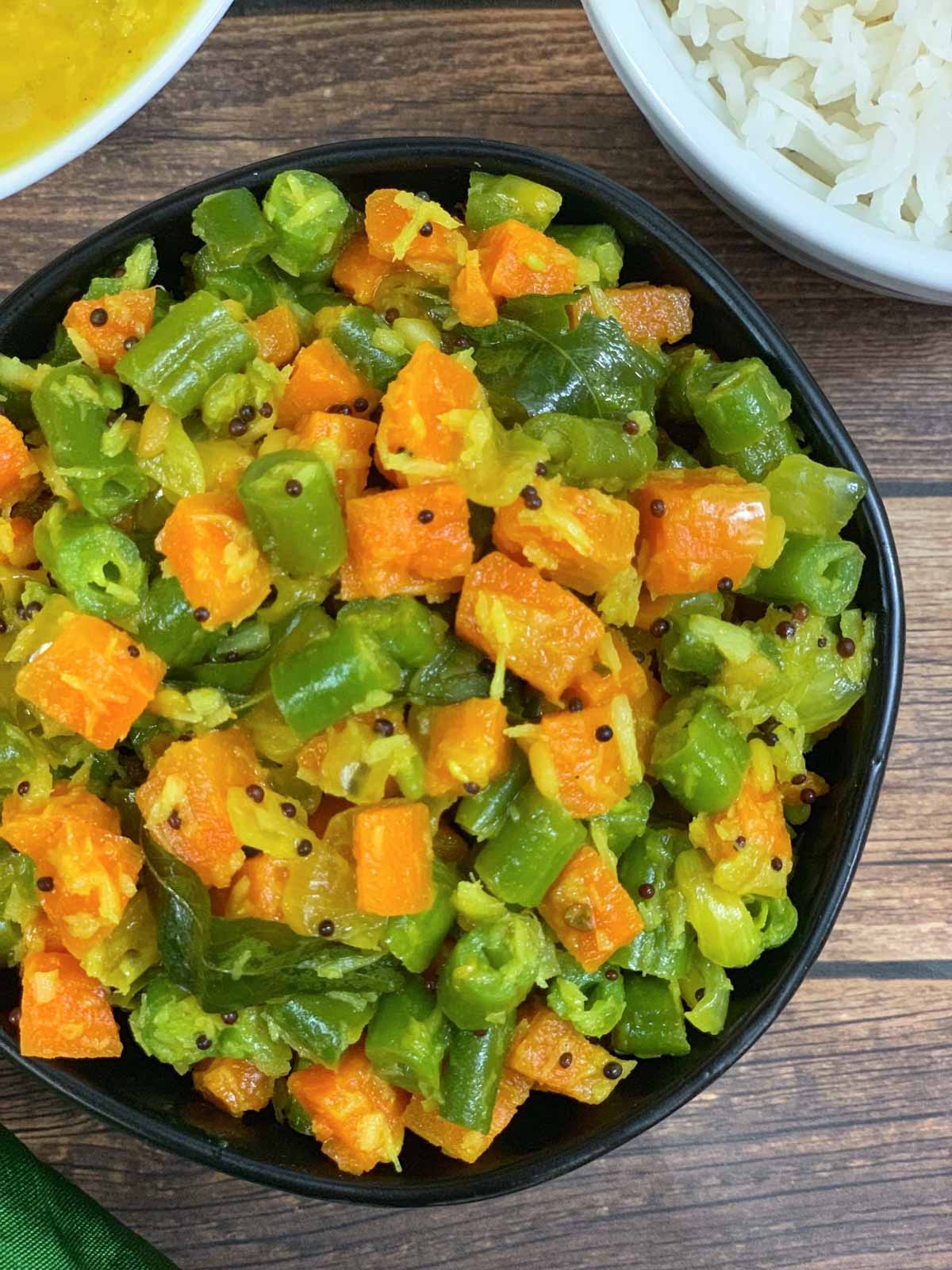 carrot beans poriyal served in a bowl with side of steamed rice and dal