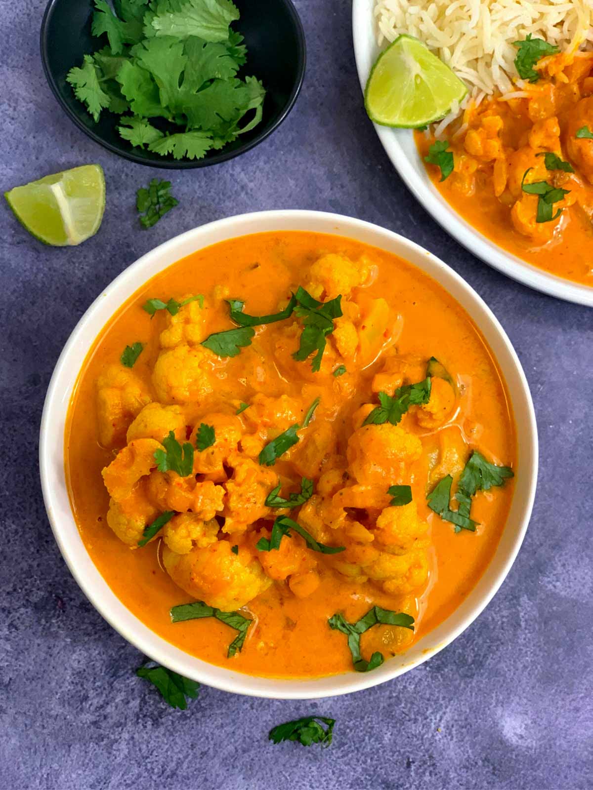 Cauliflower Coconut Milk Curry served in a bowl garnished with cilantro and lemon wedge and cilantro on the side