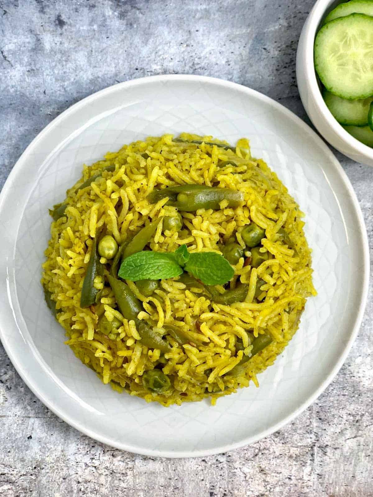 pudina rice served on a plate garnished with mint leaves with side of cucumbers
