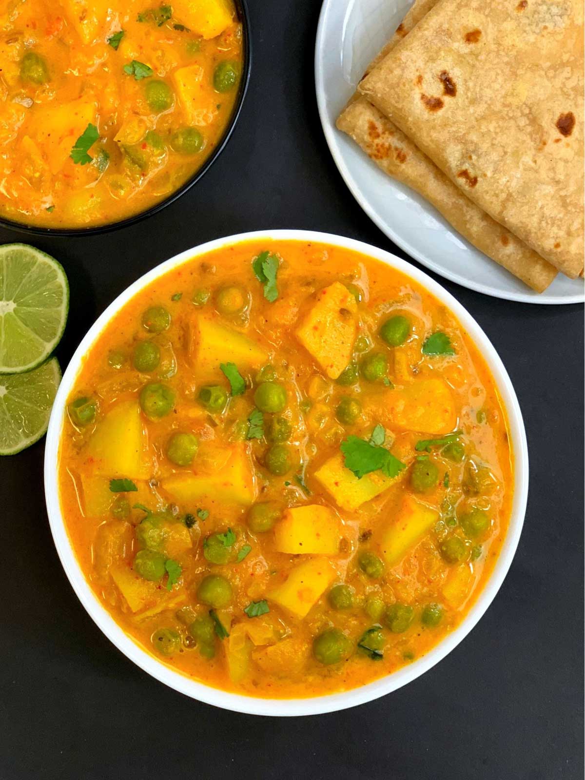 potato peas curry served in a bowl garnished with cilantro with chapati and lemon wedge on the side