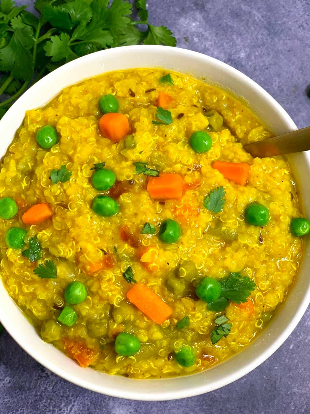 Quinoa Vegetable Khichdi served in a bowl with a spoon and cilantro on the side