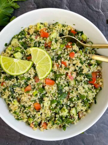 Quinoa Tabbouleh Salad served in a bowl with two spoons topped with lemon wedges