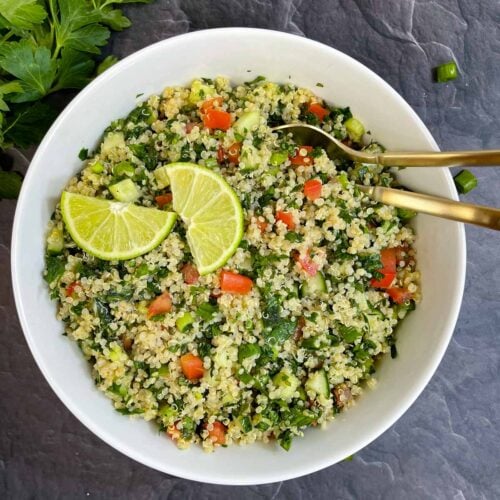 Quinoa Tabbouleh Salad served in a bowl with two spoons topped with lemon wedges