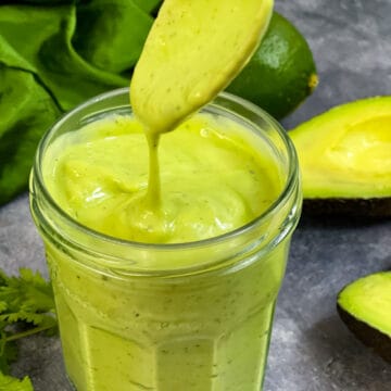 avocado cilantro lime dressing in a mason jar with some dressing dripping from a spoon