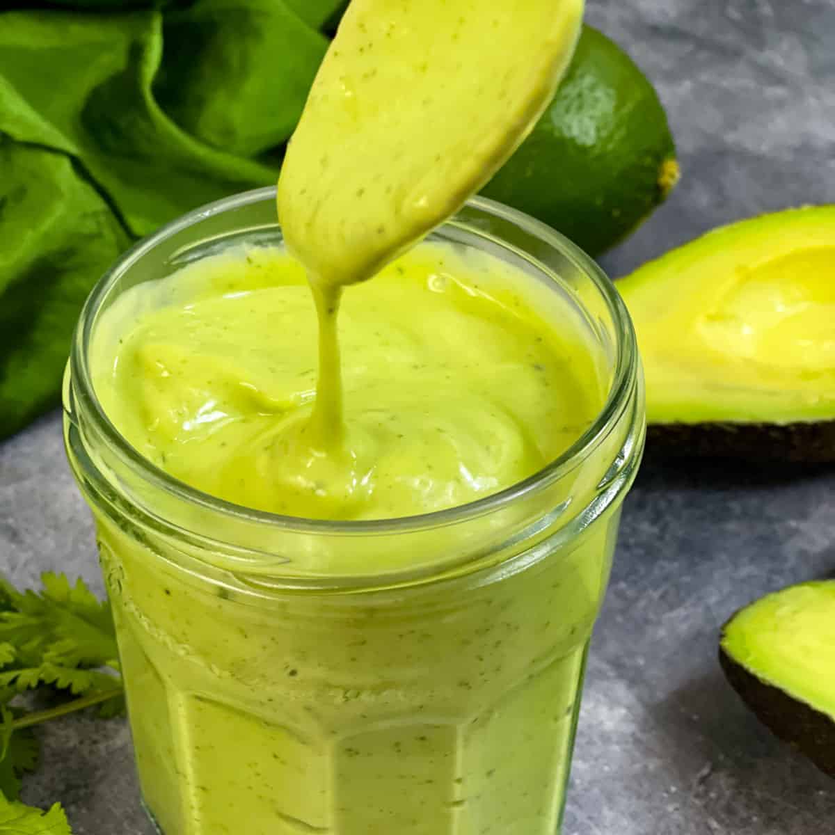 avocado cilantro dressing stored in a glass bottle and flowing from a spoon and avocado and cilantro on the side