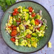 avocado corn tomato salad served in a bowl with cilantro and cut avocado on the side