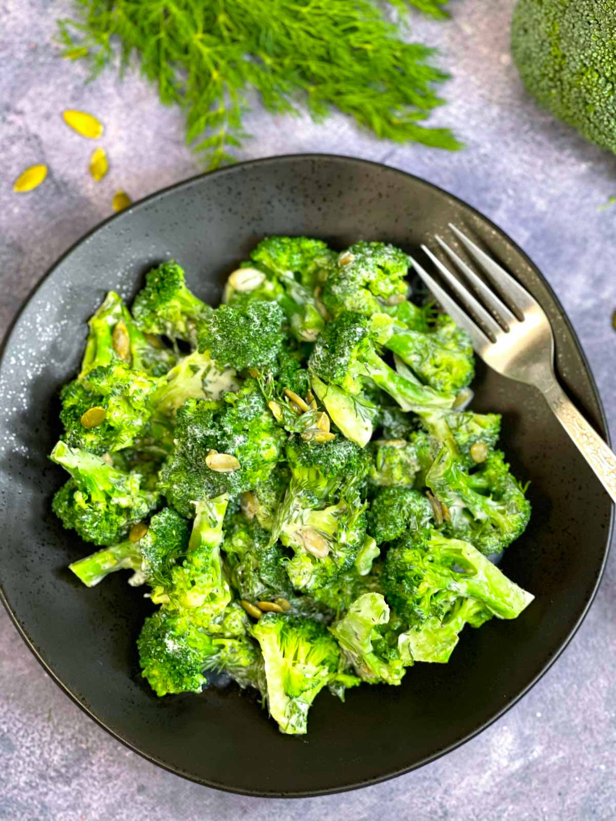 broccoli dill salad served on a plate with a fork and with dill leaves and raw broccoli on the side