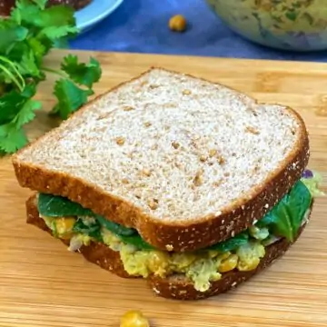 chickpea avocado salad sandwich served on wooden plank with side of cilantro