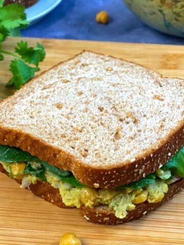chickpea avocado salad sandwich served on wooden plank with side of cilantro