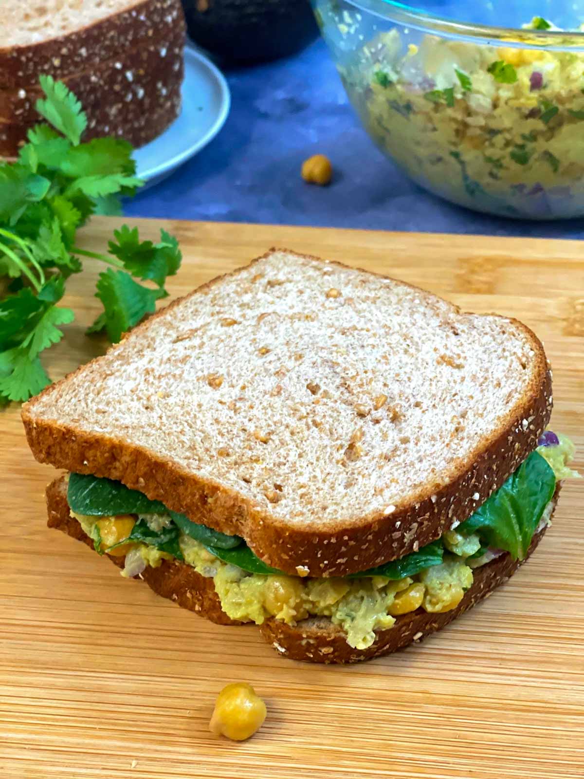 chickpea avocado salad sandwich served on wooden plank with side of cilantro