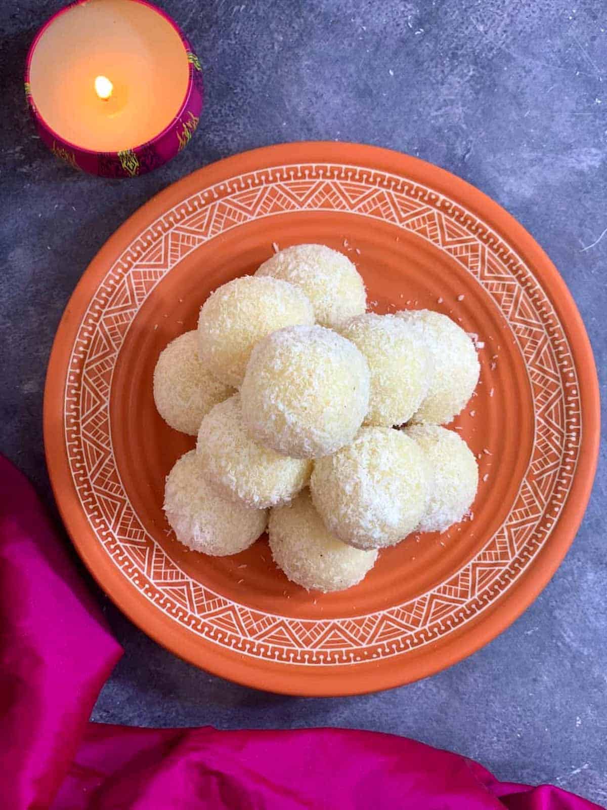 coconut ladoos on a plate with candle on the side