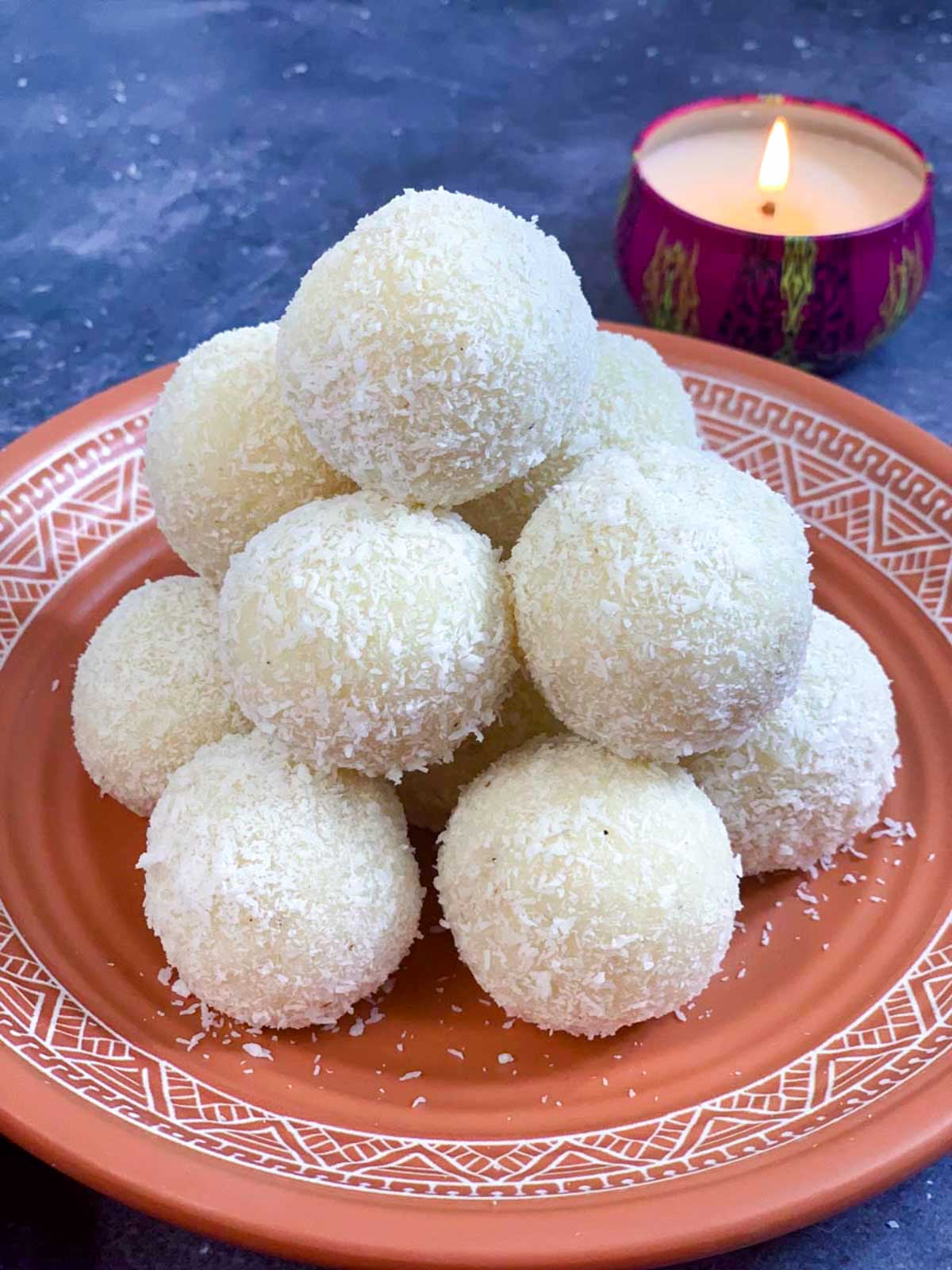 instant coconut laddos made with condensed milk placed over one another on a plate with light candle on the side