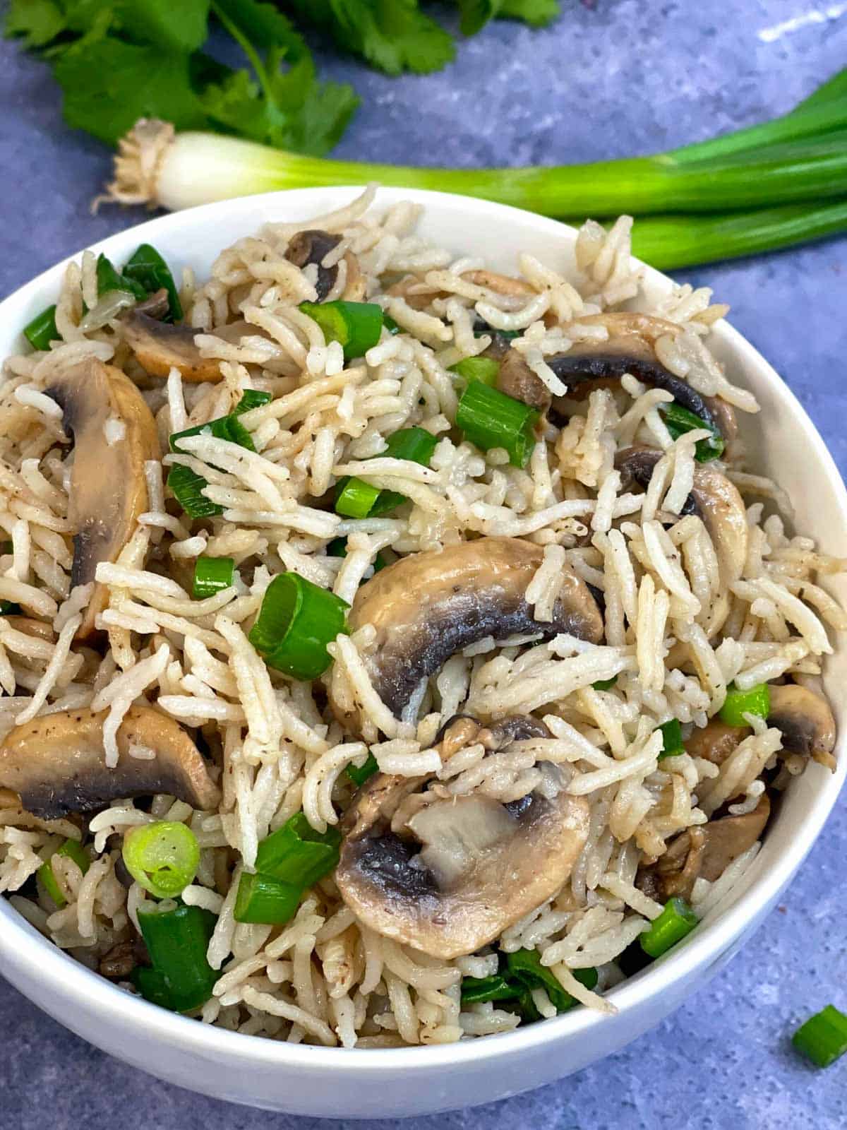 mushroom rice served in a bowl with green onions and cilantro on the side