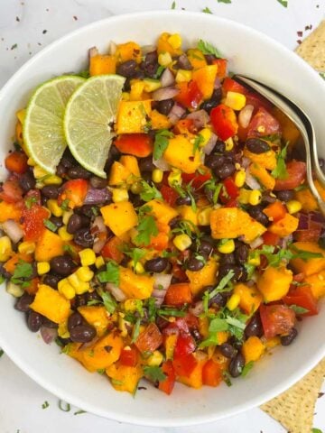 mango black bean salad served in a bowl garnished with cilantro and lime wedges with two spoons