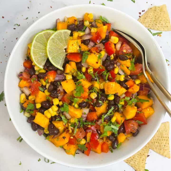 mango black bean salad served in a bowl garnished with cilantro and lime wedges with two spoons