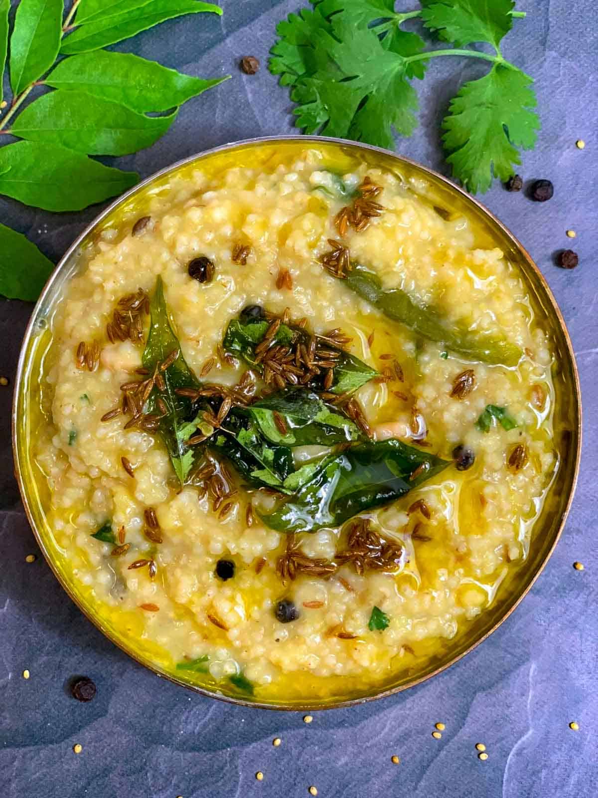 foxtail millet recipe made in the instant pot served in a copper bottom bowl and curry leaves on side