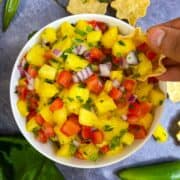 Pineapple salsa served in a bowl and scooping the salsa with chips