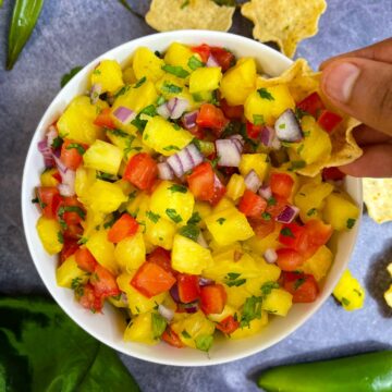 Pineapple salsa served in a bowl and scooping the salsa with chips