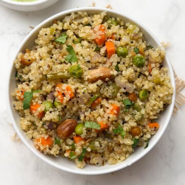 Quinoa upma served in a white bowl with coconut chutney on the side.